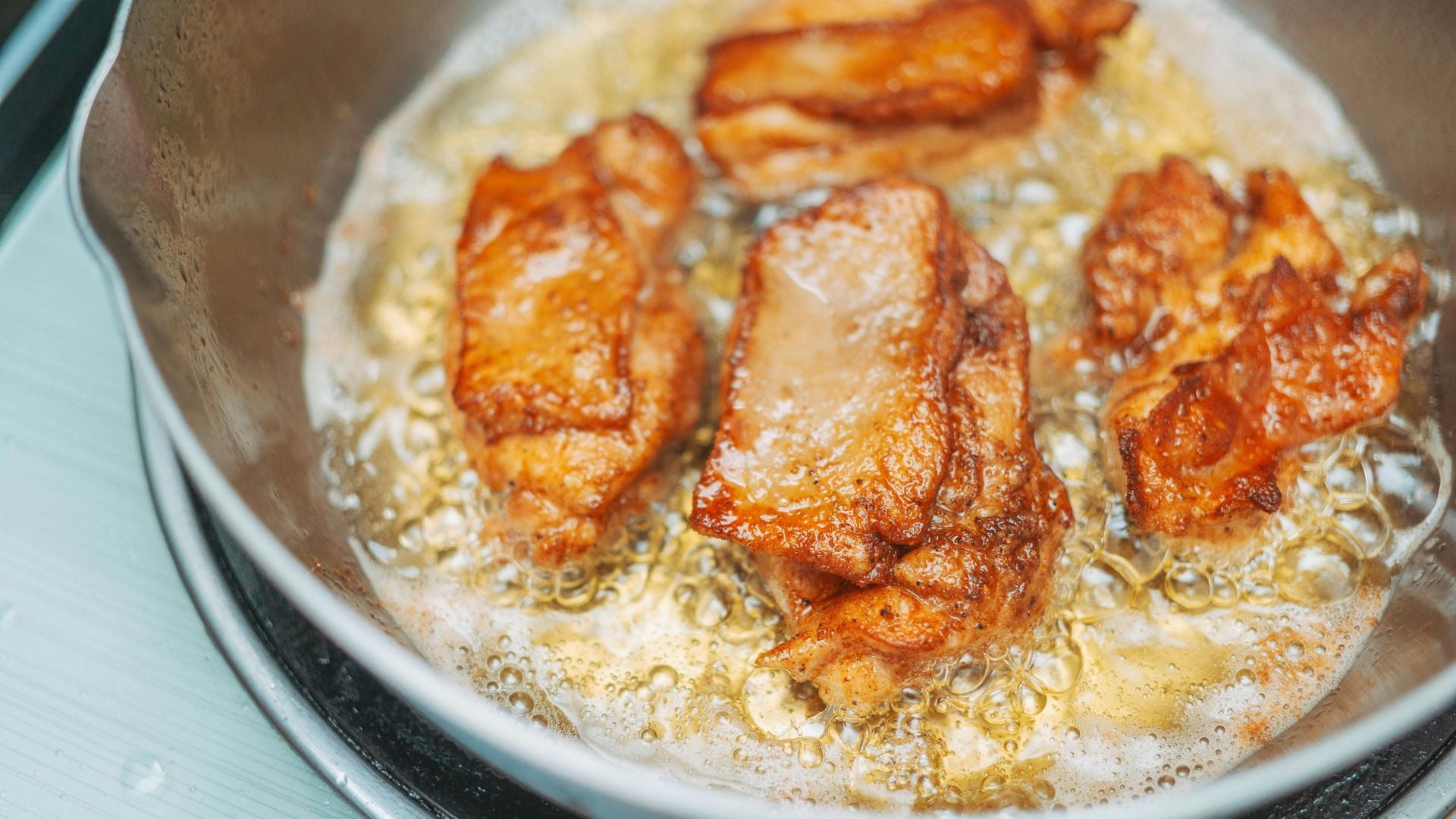 Pieces of chicken being pan-fried with a golden crust on top.