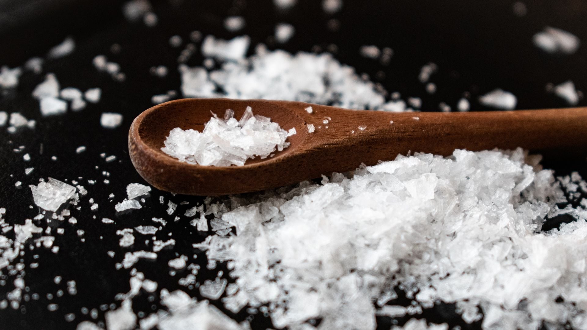 A picture of salt with a wooden spoon on a dark surface